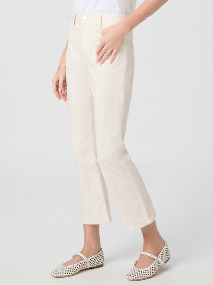A person wearing the Paige Mason Crop Bootcut Jean in Tonal Stripe with a subtle bootcut flare and white flats stands with one hand in a front pocket against a plain background.
