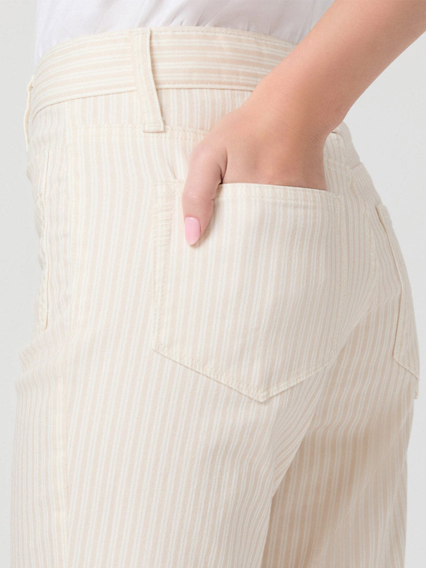 Someone wearing the Paige Mason Crop Bootcut Jean in Tonal Stripe, featuring light beige and white stripes in ecru denim, with one hand in the front pocket.