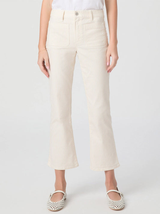 Wearing Paige Mason Crop Bootcut Jean in Tonal Stripe, a white shirt, and white cutout flat shoes, the person stands against a plain light background.