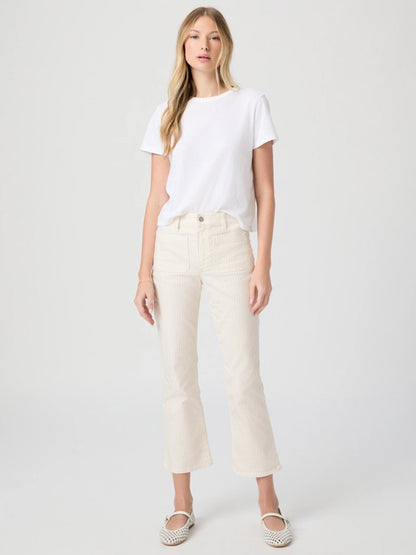 A woman stands against a plain background wearing a white t-shirt, slip-on shoes, and Paige Mason Crop Bootcut Jean in Tonal Stripe.