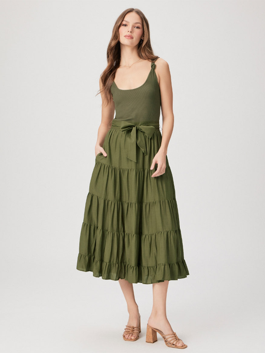 A woman stands wearing a green Paige Samosa Dress in Dark Olive with strappy heels.