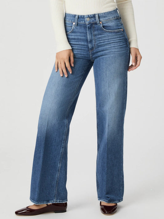 A person wears Paige Sasha 32" Wide Leg Jean in Stefania Distressed, paired with a white ribbed long-sleeve top and brown shoes, standing against a plain background.