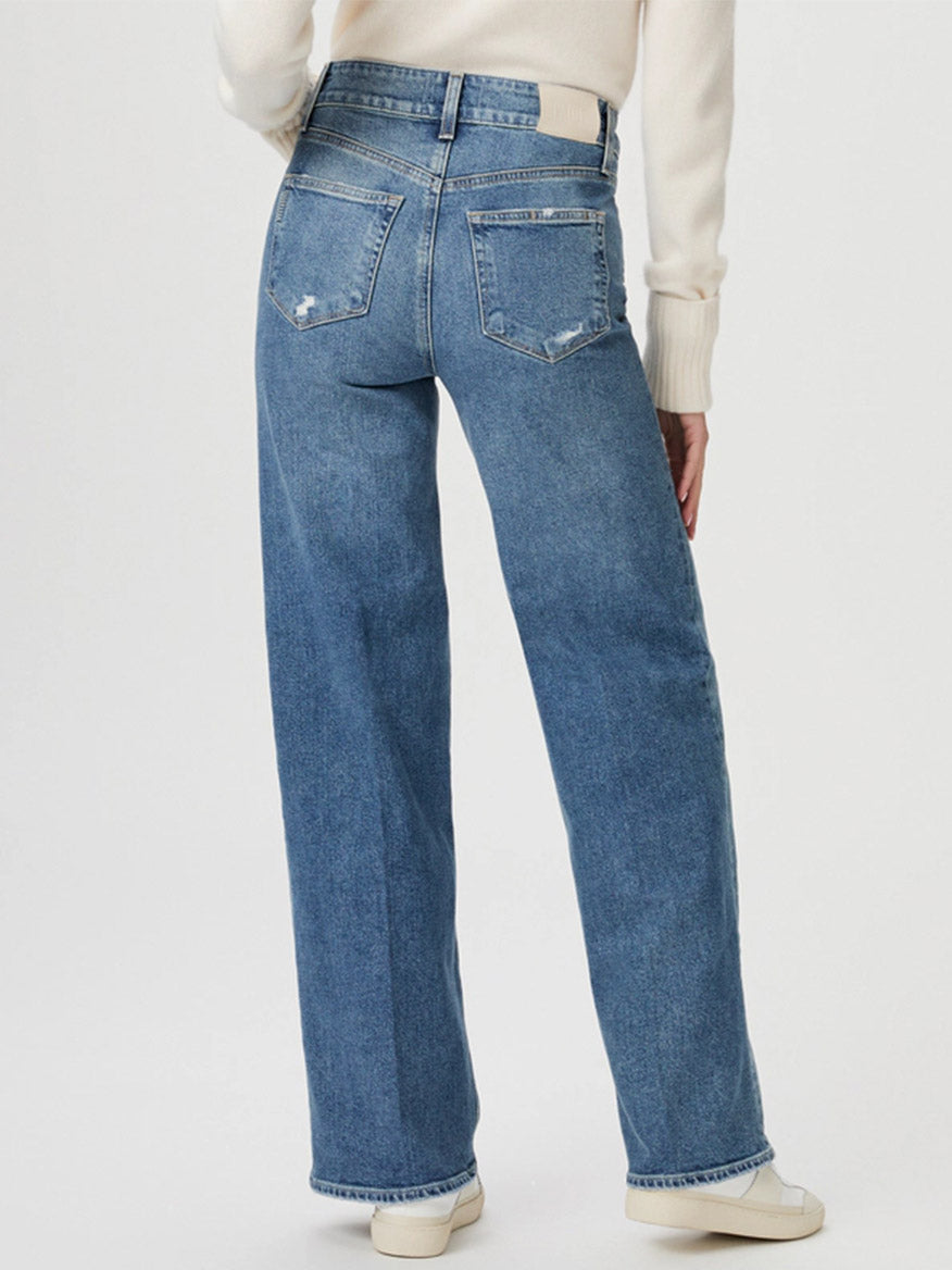 Person wearing the Paige Sasha 32" Wide Leg Jean in Storybook Distressed, featuring high-rise wide-leg blue jeans and a white sweater, standing with their back to the camera.