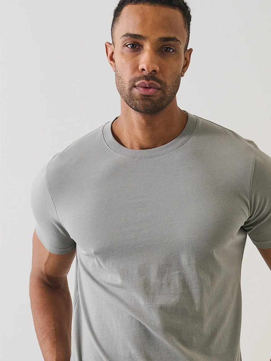 A man stands against a plain white background, wearing the Patrick Assaraf Organic Pima Cotton High Neck T-Shirt in Pewter and looking directly at the camera.