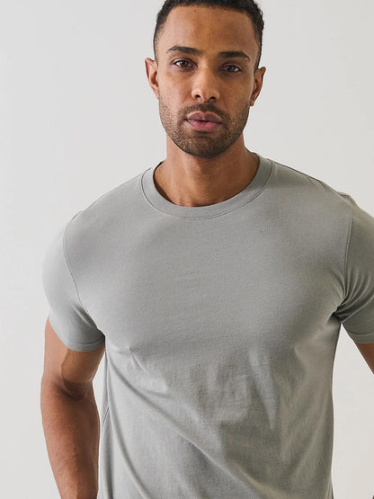 A man stands against a plain white background, wearing the Patrick Assaraf Organic Pima Cotton High Neck T-Shirt in Pewter and looking directly at the camera.