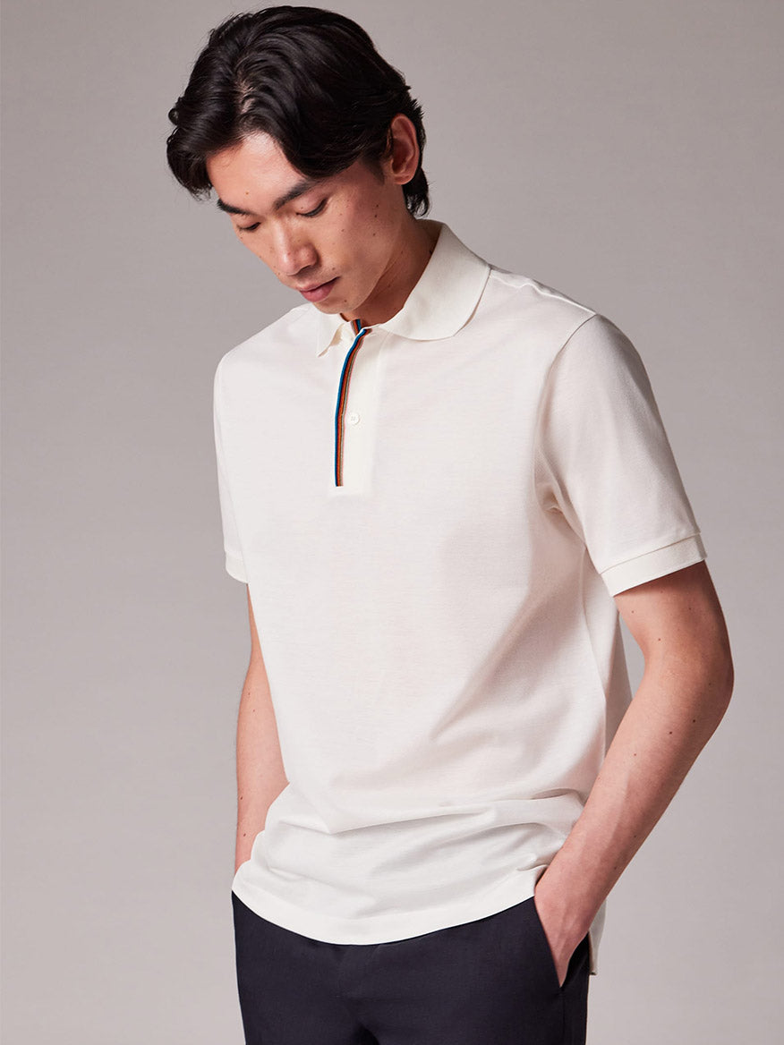 A person stands with hands in pockets, looking down, wearing a Paul Smith Signature Stripe Trim Polo Shirt in White.