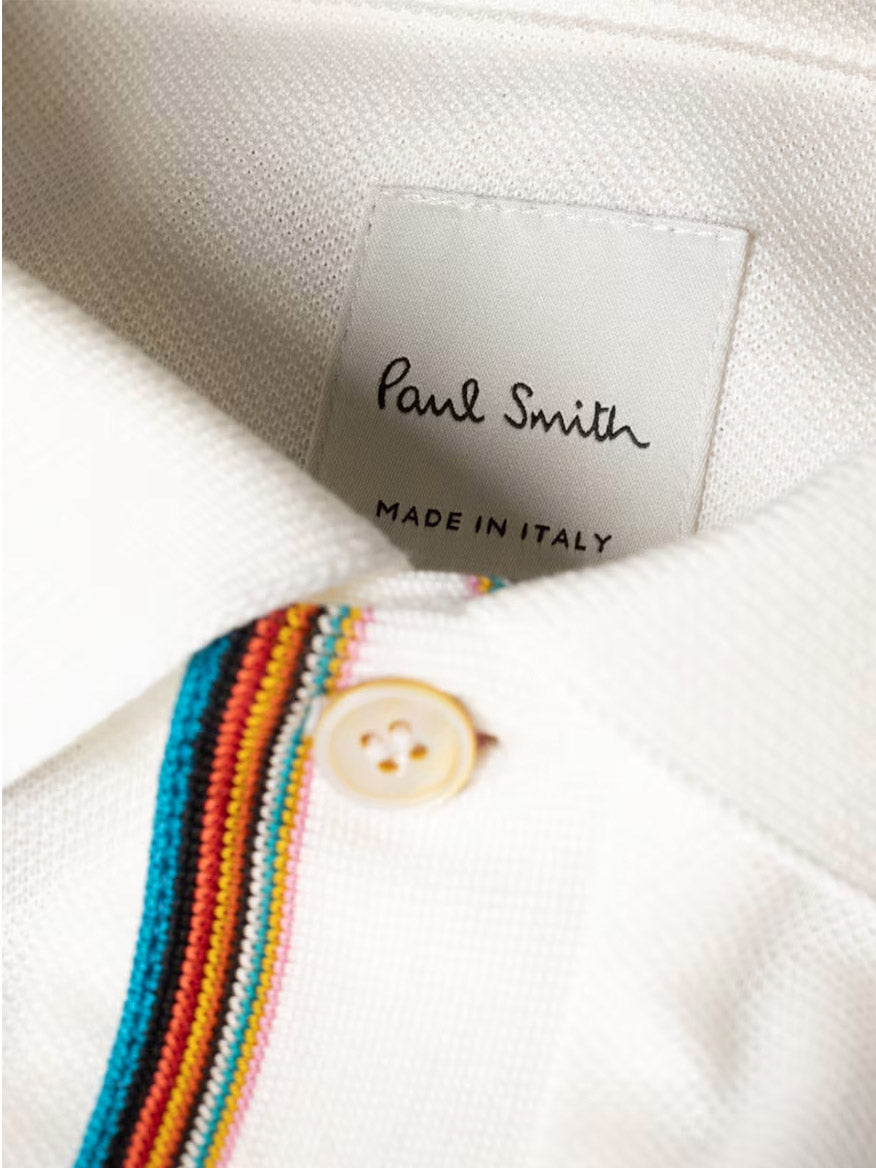 Close-up of the Paul Smith Signature Stripe Trim Polo Shirt in white, featuring a beige button and Signature Stripe detailing near the collar. The label reads "Paul Smith Made in Italy.