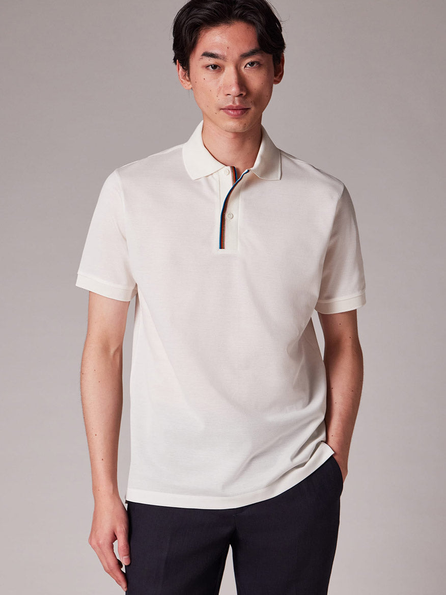 A person stands facing forward, wearing the Paul Smith Signature Stripe Trim Polo Shirt in White with dark pants, set against a plain background.