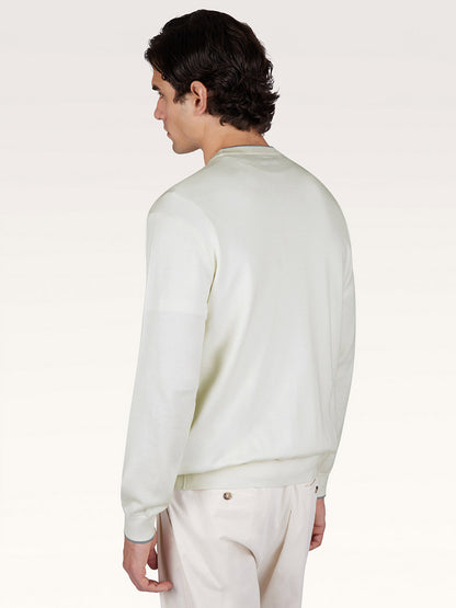 A man with dark hair is standing and facing away from the camera, wearing a Paul & Shark Crew‑Neck Sweater With Aqualeather Suede Details in White and light pants.