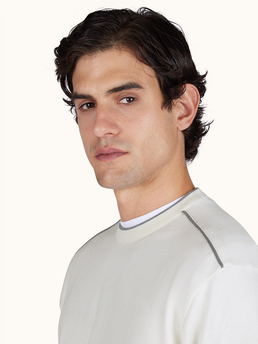 A man with dark, wavy hair wears the Paul & Shark Crew‑Neck Sweater With Aqualeather Suede Details in white, looking toward the camera with a neutral expression against a plain background.