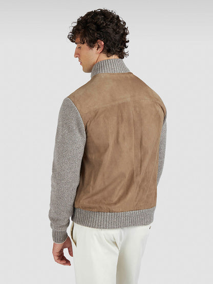 A man faces away, wearing the Paul & Shark Hybrid Zip-Up Cardigan in Natural with gray knit sleeves and collar, paired with white pants, against a plain light background.