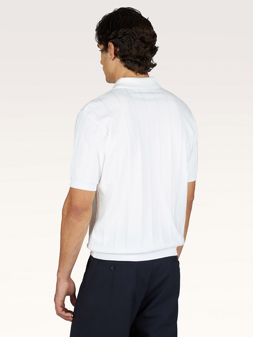 Man standing with his back to the camera, wearing a Paul & Shark Polo in Piuma Cotton in Blanc de Blanc and dark pants against a plain light background.