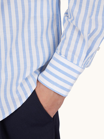 Someone wears the Paul & Shark Cotton Poplin Shirt With Striped Pattern in White/Blue, featuring vertical stripes, a button-down collar, visible sleeve cuff, and has a hand in the pocket of dark pants.