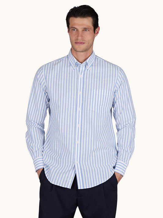 A man wearing the Paul & Shark Cotton Poplin Shirt with a white and blue striped pattern, button-down collar, and long sleeves pairs it with dark pants as he stands hands in pockets.
