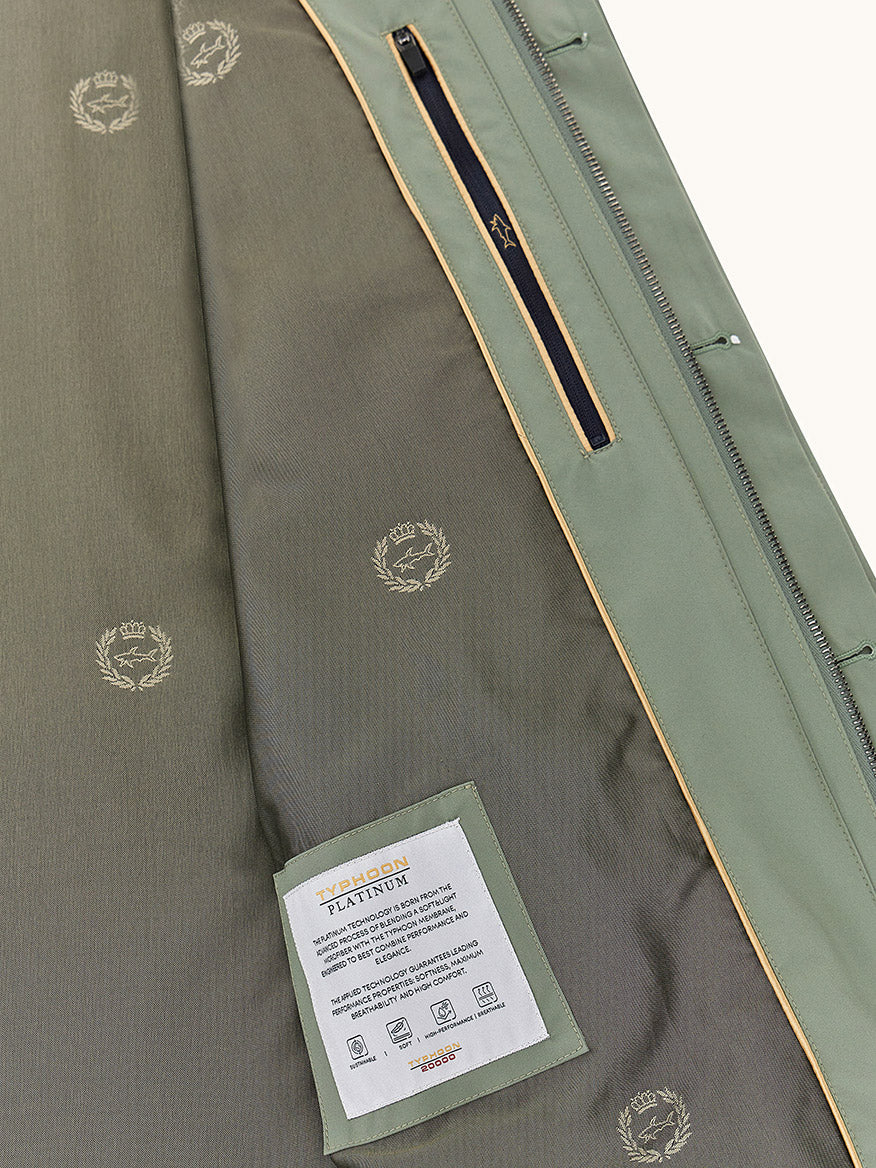Close-up of the Paul & Shark Typhoon® Platinum Car Coat with Aqualeather suede details in olive, showing its patterned lining, zippered pocket, and a rectangular care label with text and symbols.