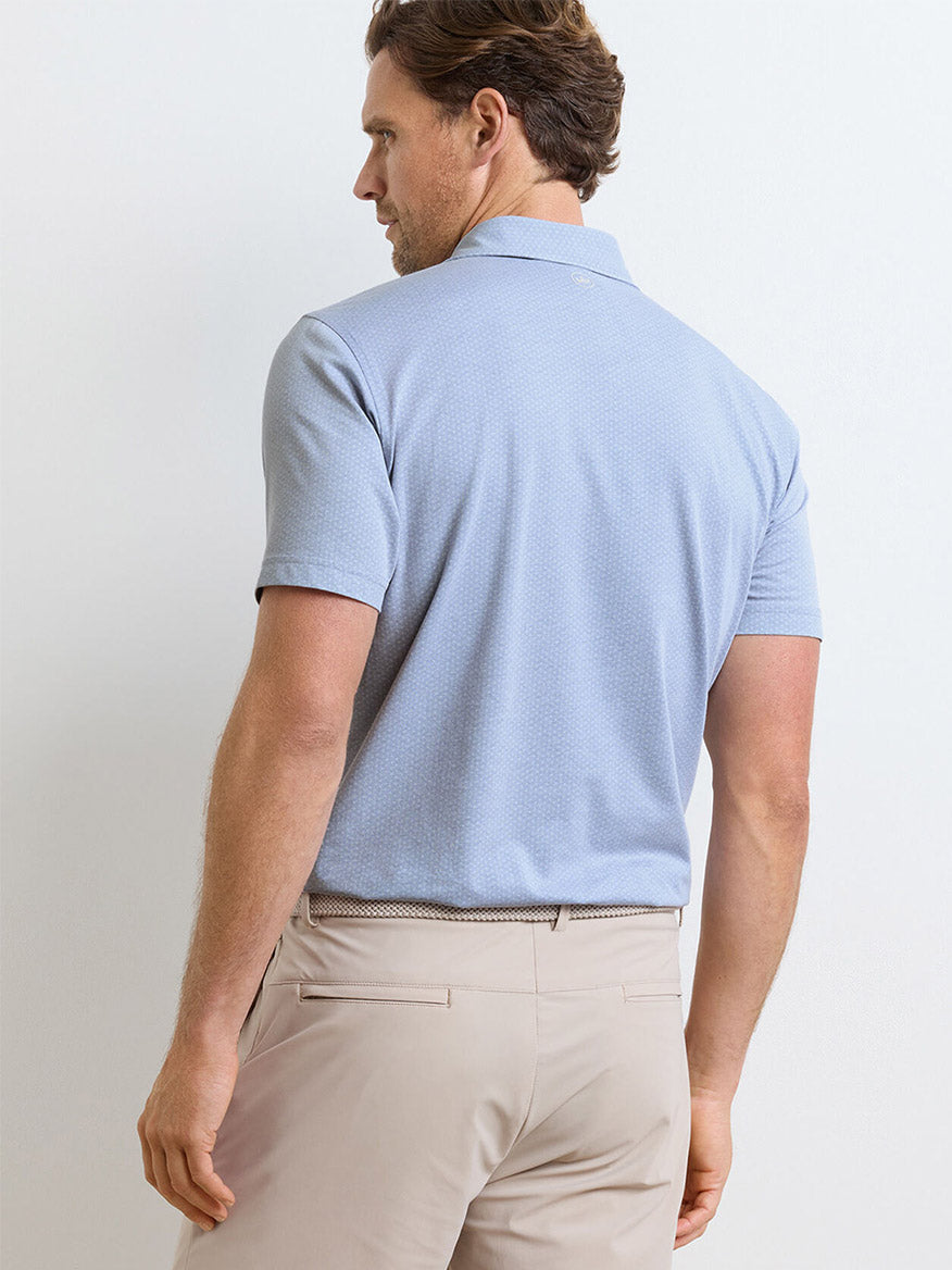 A man is seen from the back wearing the Peter Millar Albatross Diamond Cotton-Blend Piqué Polo in Dusk Blue and beige pants, standing against a plain light-colored background.