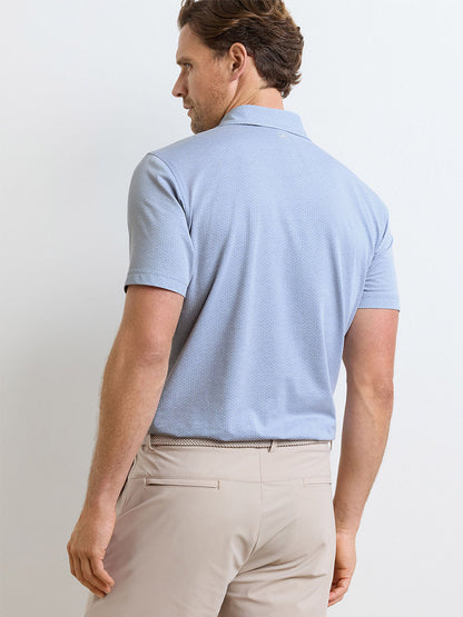 A man is seen from the back wearing the Peter Millar Albatross Diamond Cotton-Blend Piqué Polo in Dusk Blue and beige pants, standing against a plain light-colored background.