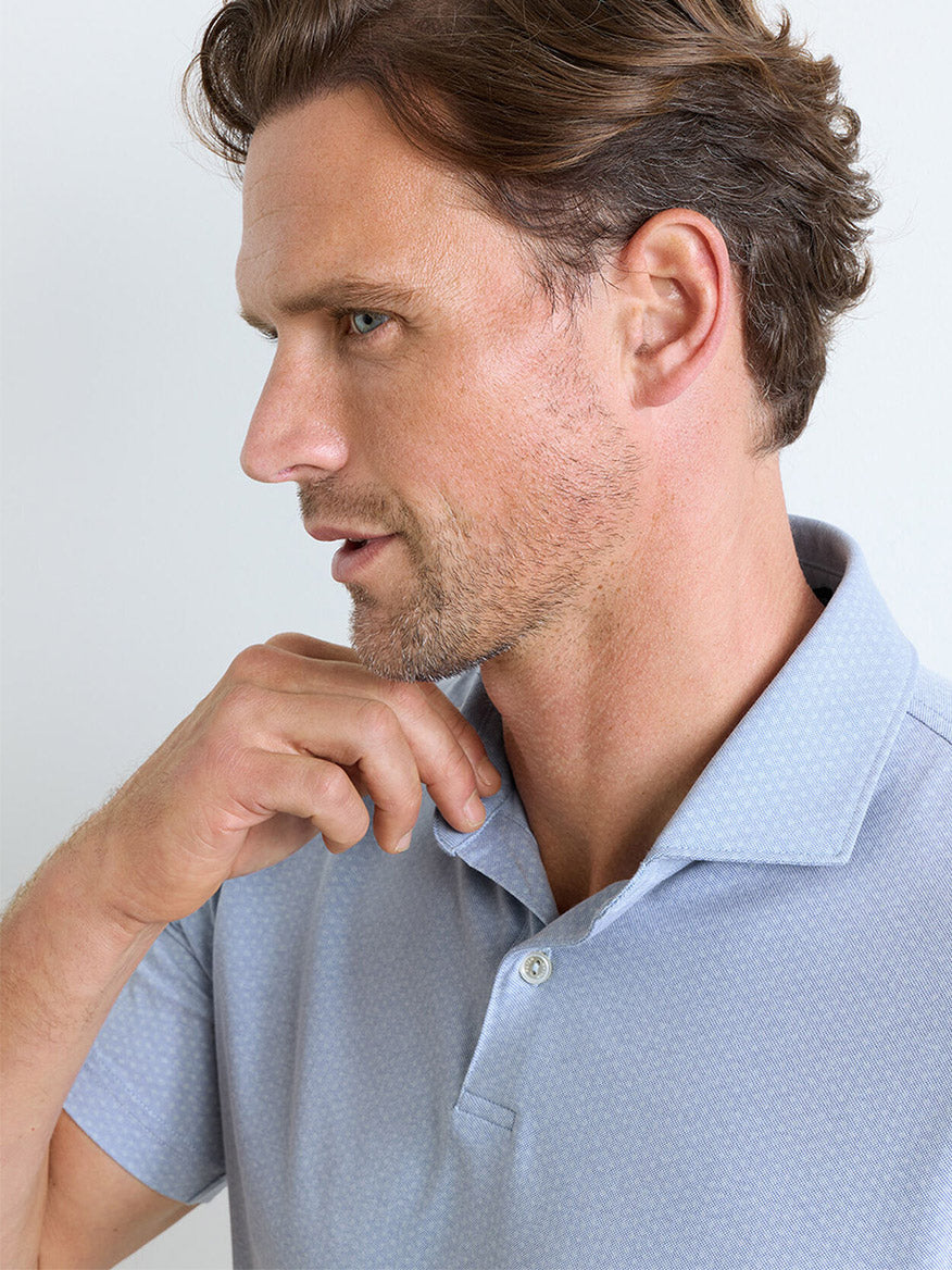 Man in a Dusk Blue Peter Millar Albatross Diamond Cotton-Blend Piqué Polo, tailored fit, shown from the shoulders up against a plain background, looking to the side with one hand touching his neck.
