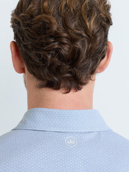 A man with brown wavy hair is shown from behind, wearing a Peter Millar Albatross Diamond Cotton-Blend Piqué Polo in Dusk Blue, featuring a tailored fit and a small white crown emblem on the back.