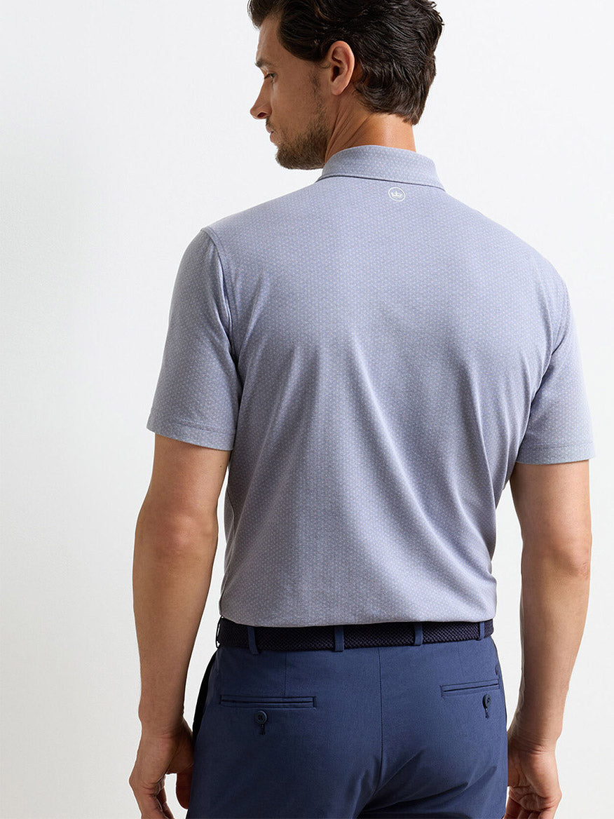 A man with short dark hair is shown from the back, wearing a Peter Millar Albatross Diamond Cotton-Blend Piqué Polo in navy, tailored fit, tucked into navy dress pants with a matching belt.