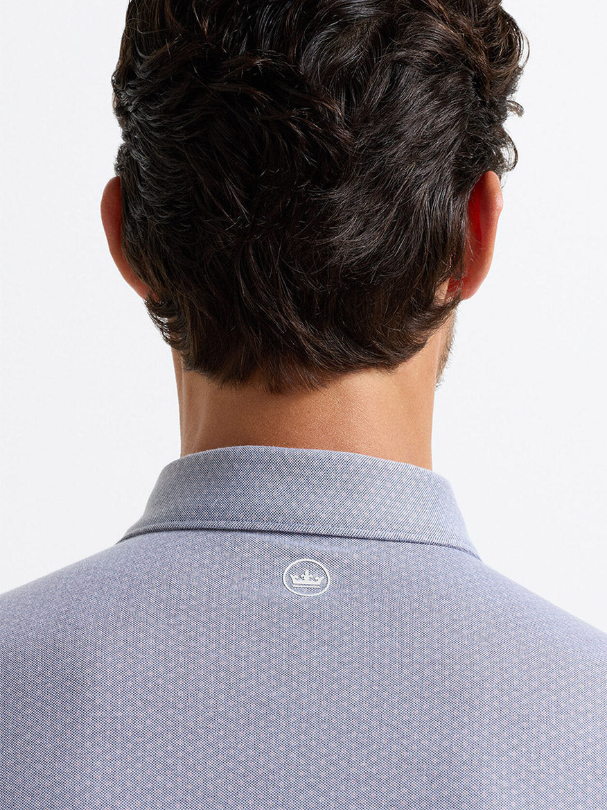 A man is shown from behind wearing the Peter Millar Albatross Diamond Cotton-Blend Piqué Polo in navy, featuring a small white crown logo at the top center of the back.