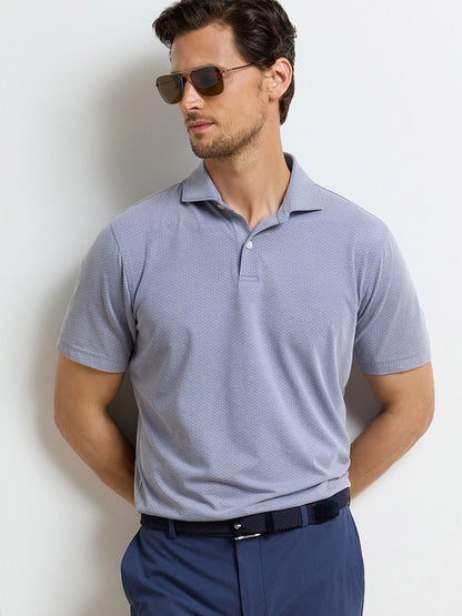 Man wearing sunglasses and the Peter Millar Albatross Diamond Cotton-Blend Piqué Polo in Navy, styled in a tailored fit with navy pants, stands against a white background with his hands behind his back.