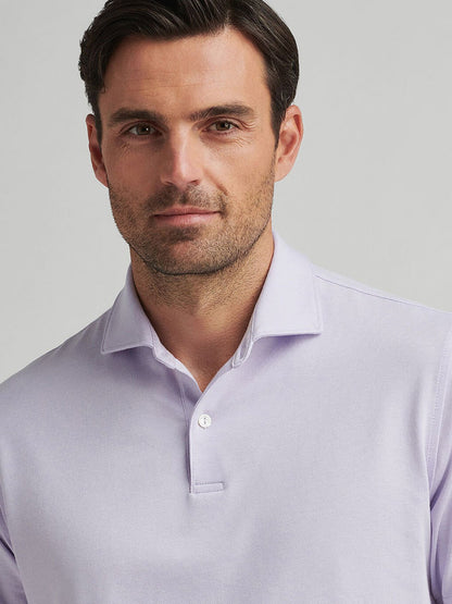 A man wearing the Peter Millar Albatross Cotton Blend Piqué Polo in Lavender Moon looks at the camera against a gray background.