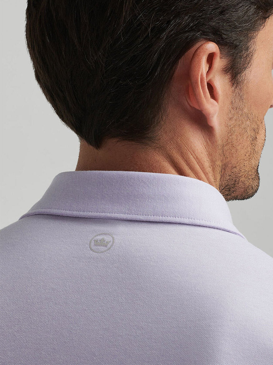 A man is seen from behind wearing the Peter Millar Albatross Cotton Blend Piqué Polo in Lavender Moon, crafted from soft pima cotton with an Oxford piqué knit, featuring four-way stretch and a small crown logo on the back.