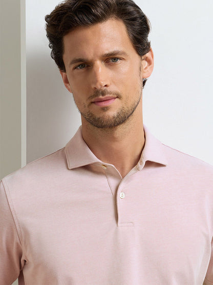 A man with short brown hair and light stubble wears the Peter Millar Albatross Cotton Blend Piqué Polo in Faded Scarlet, looking at the camera against a plain light background.