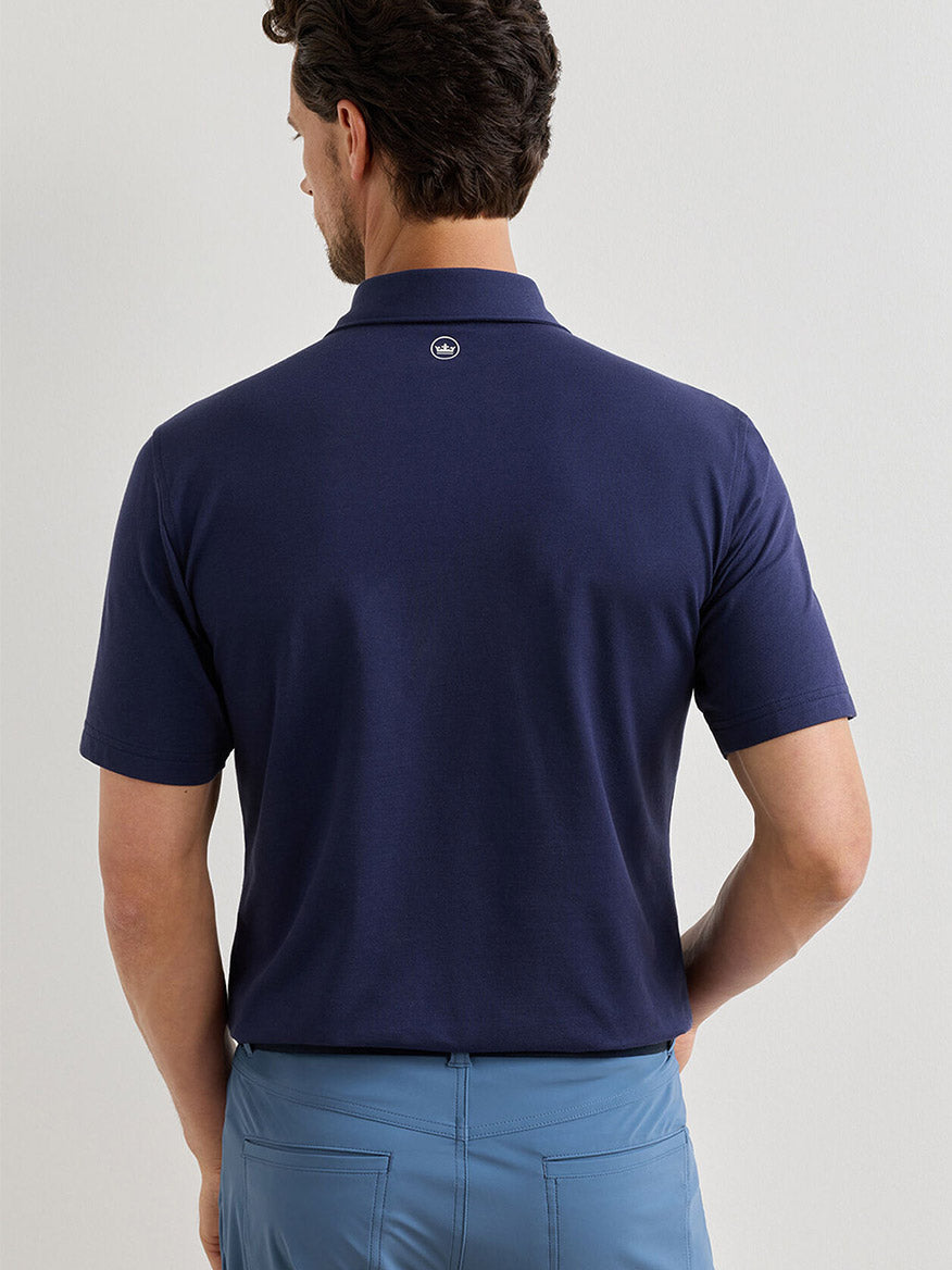 A man with short dark hair is seen from behind, wearing a Peter Millar Albatross Cotton Blend Piqué Polo in navy and light blue pants.