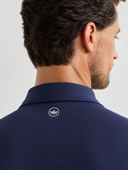 Man shown from behind wearing the Peter Millar Albatross Cotton Blend Piqué Polo in navy, featuring a small white crown logo on the upper back.