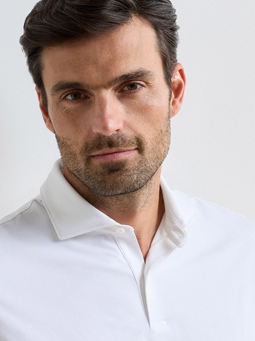 A man with dark hair and a beard, wearing the Peter Millar Albatross Cotton Blend Piqué Polo in White, looks toward the camera against a plain light background.