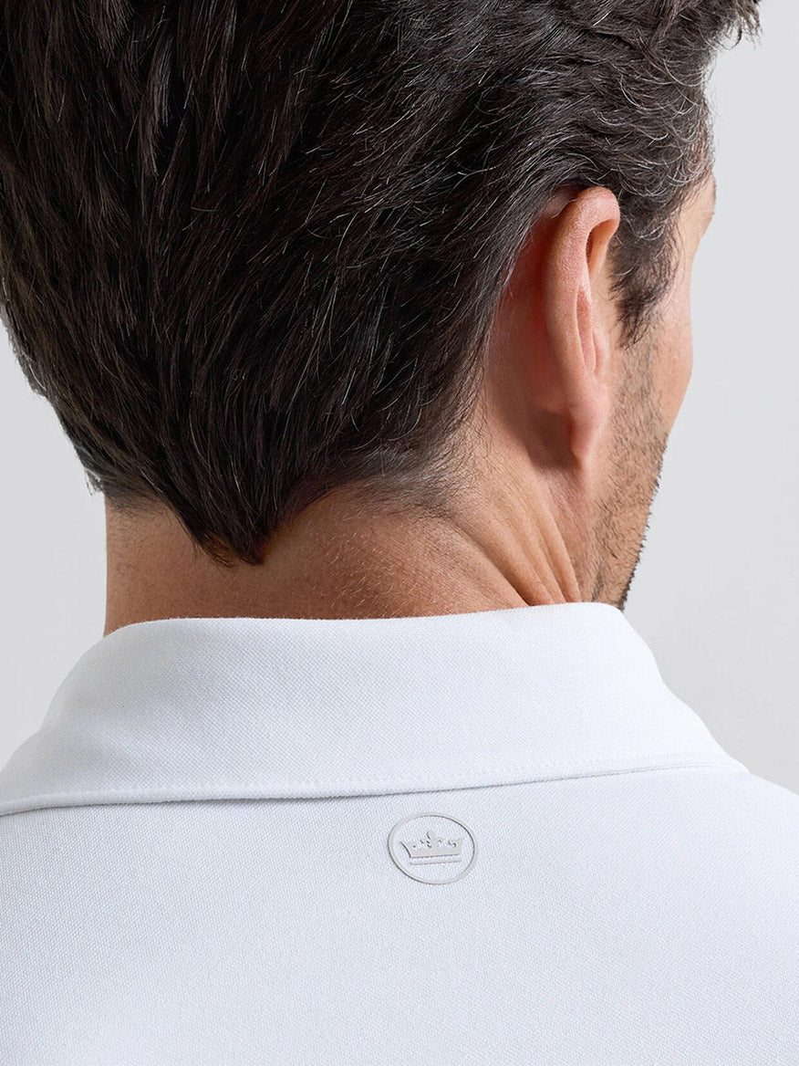 A man with short dark hair is seen from behind wearing the Peter Millar Albatross Cotton Blend Piqué Polo in White, featuring a soft Oxford piqué knit and a small circular logo at the back of the collar.