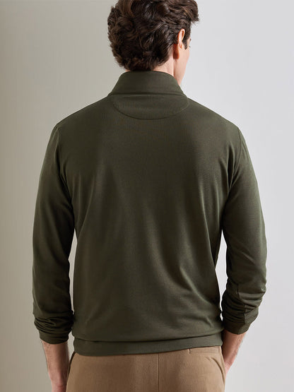 A man stands facing away, wearing the Peter Millar Albatross Cotton-Blend Piqué Quarter-Zip in Dark Olive and tan pants, against a plain light-colored wall.