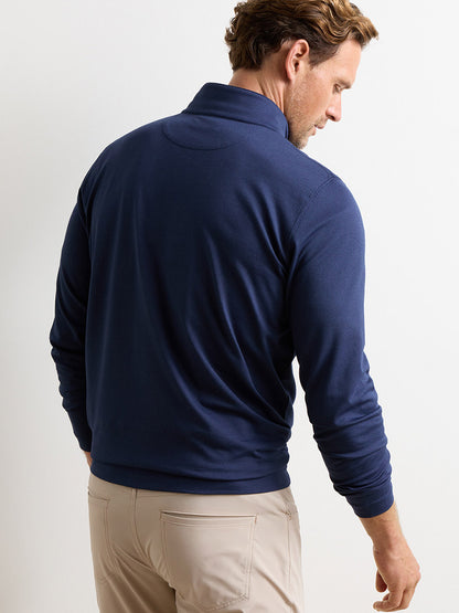 A man stands facing away, wearing the Peter Millar Albatross Cotton-Blend Piqué Quarter-Zip in Navy and light beige pants against a plain white background.