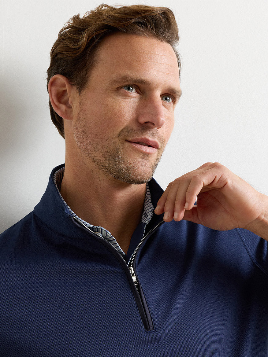 Man with short brown hair wearing the Peter Millar Albatross Cotton-Blend Piqué Quarter-Zip in Navy over a light patterned shirt, looking slightly to the side while holding the zipper.