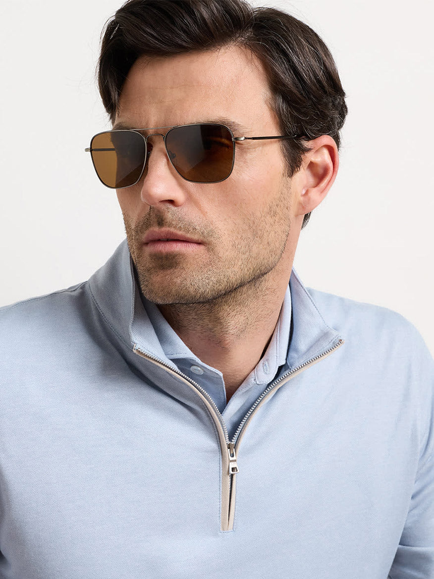 A man wearing the Peter Millar Albatross Cotton-Blend Piqué Quarter-Zip in Windy Blue and brown-tinted sunglasses looks to the side against a plain background.