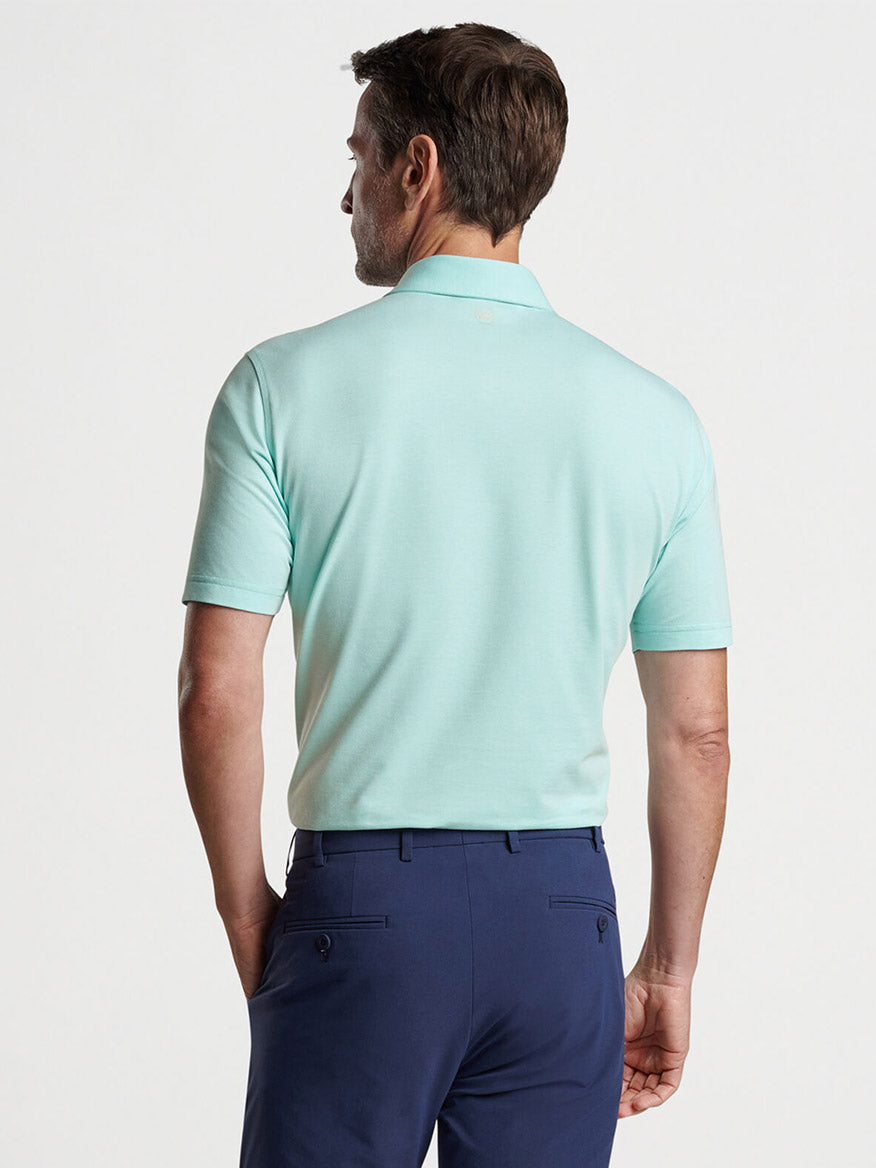 Man wearing a Peter Millar Albatross Cotton Blend Piqué Polo in Iced Aqua and navy trousers viewed from behind.