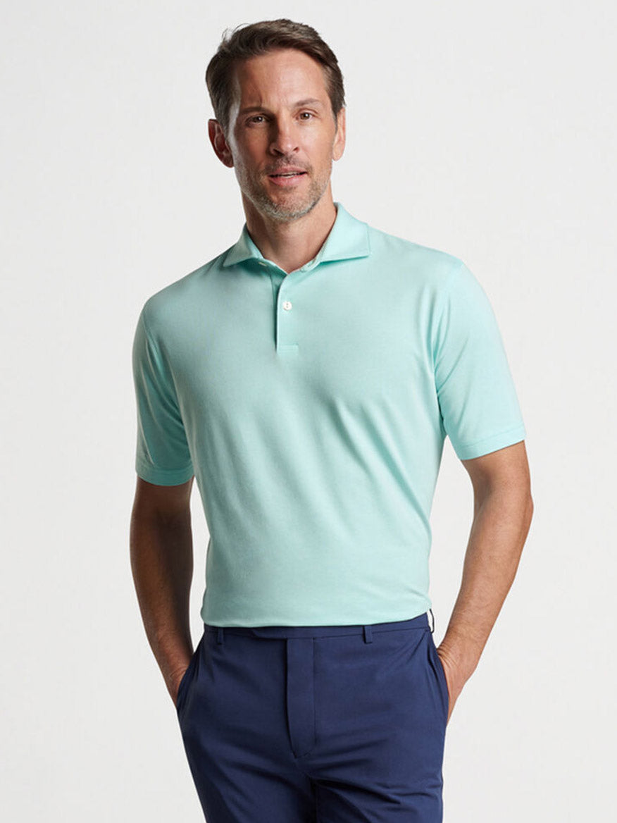 A man wearing a light green Peter Millar Albatross Cotton Blend Piqué Polo in Iced Aqua and navy trousers stands posing for the camera.
