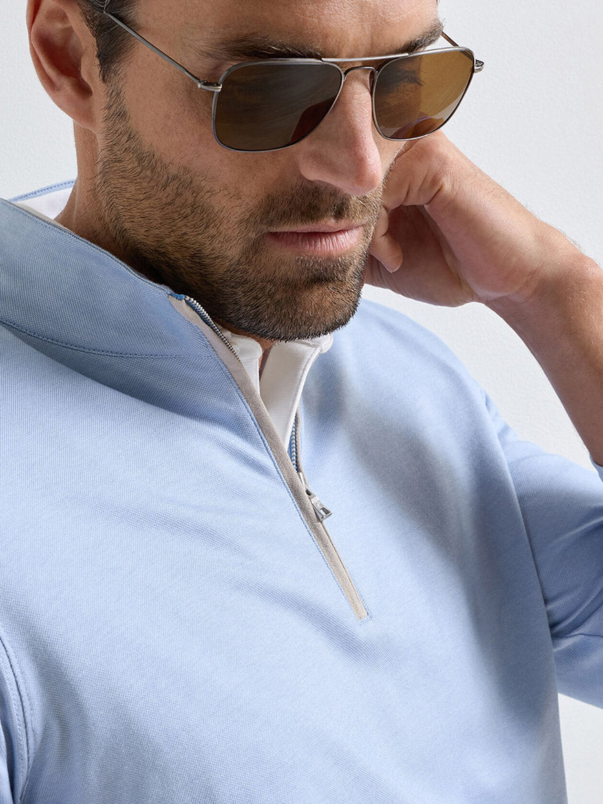 A man wearing sunglasses and the Peter Millar Albatross Cotton-Blend Piqué Quarter-Zip in Dusk Blue looks down while touching his neck.