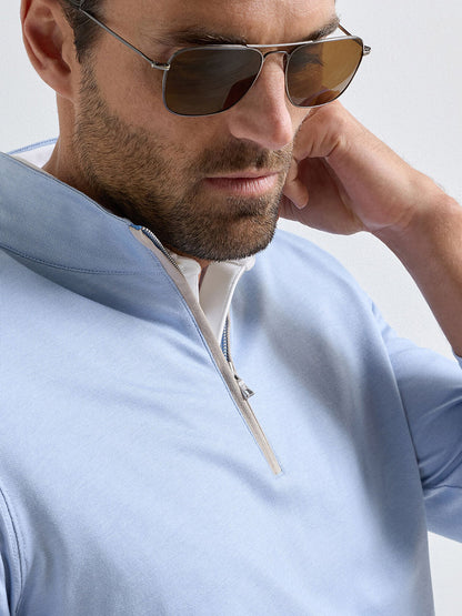 A man wearing sunglasses and the Peter Millar Albatross Cotton-Blend Piqué Quarter-Zip in Dusk Blue looks down while touching his neck.