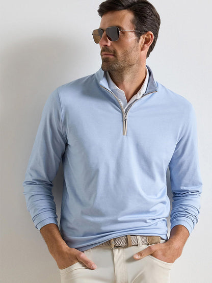 A man wearing sunglasses, beige pants, a patterned belt, and the Peter Millar Albatross Cotton-Blend Piqué Quarter-Zip in Dusk Blue stands against a plain white background.