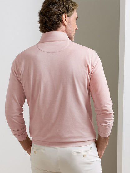 A man faces away from the camera, wearing the Peter Millar Albatross Cotton-Blend Piqué Quarter-Zip in Faded Scarlet and white pants, set against a neutral background.
