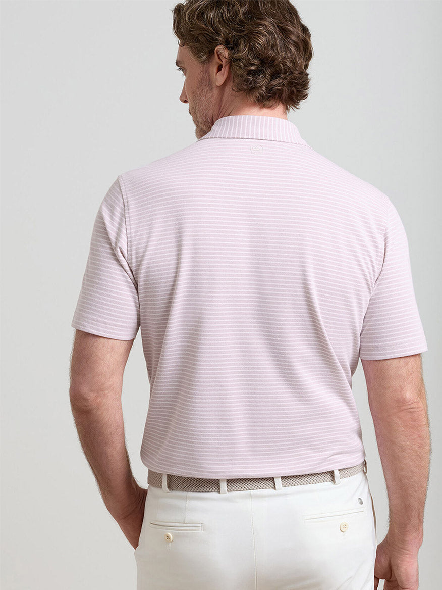 A man is seen from behind, wearing a Peter Millar Albatross Stripe Cotton-Blend Piqué Polo in Faded Scarlet, paired with white pants and a white belt.