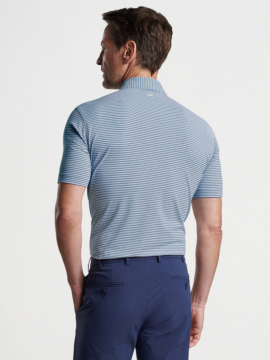 Man wearing a Peter Millar Alto Performance Jersey Polo in White/Navy and blue trousers, viewed from behind.