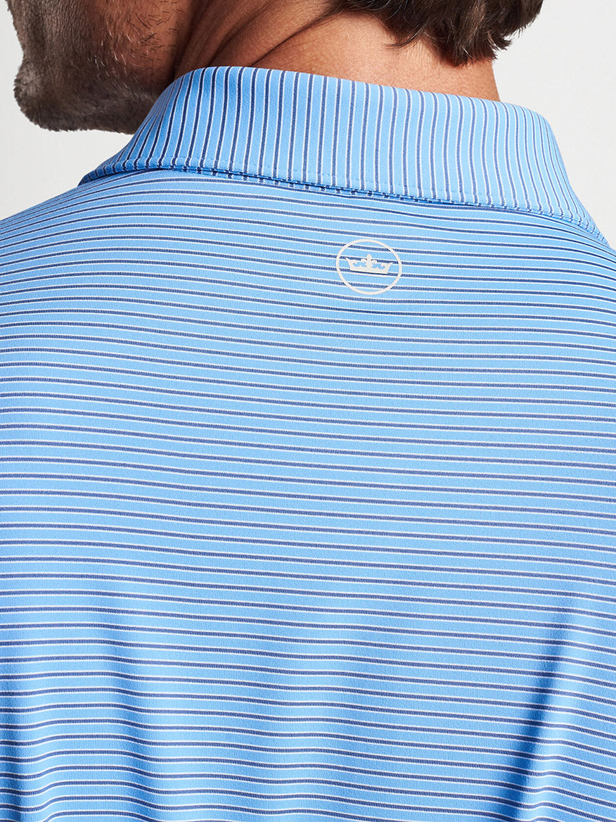 Man wearing a striped blue and white Peter Millar Ambrose Performance Jersey Polo in Regatta Blue with a logo on the back of the collar.