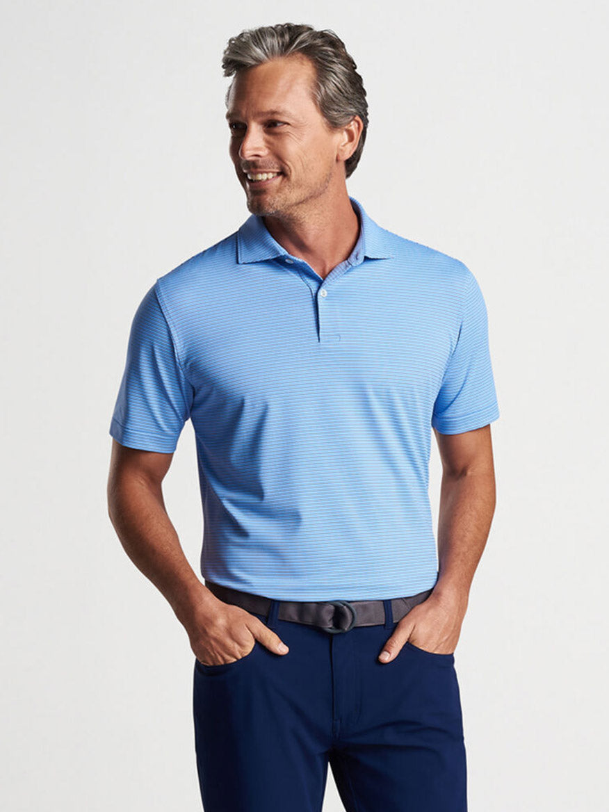 A man smiling and posing in a Peter Millar Ambrose Performance Jersey Polo in Regatta Blue and navy trousers.