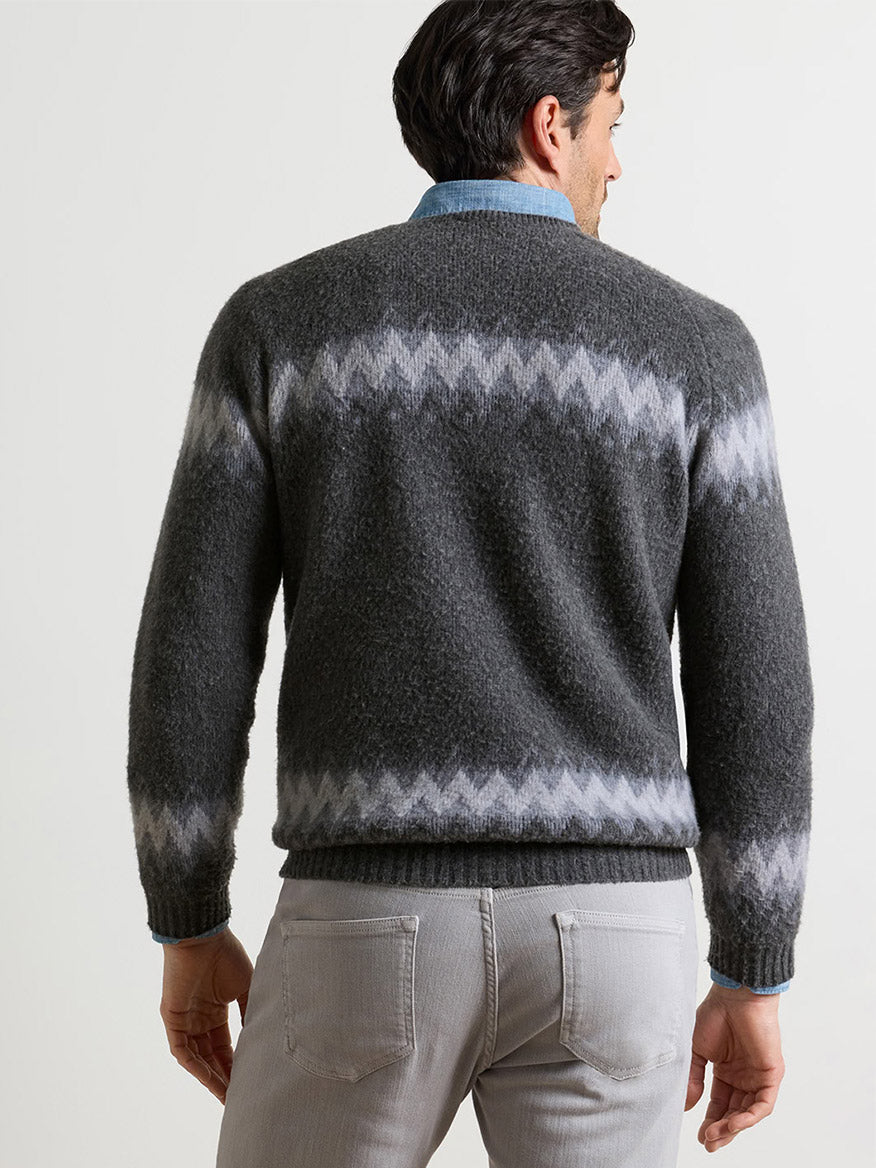 A person wearing a grey Peter Millar Après-Ski Crewneck Sweater in Fossil with a zig-zag pattern across the chest and cuffs, layered over a blue collared shirt.