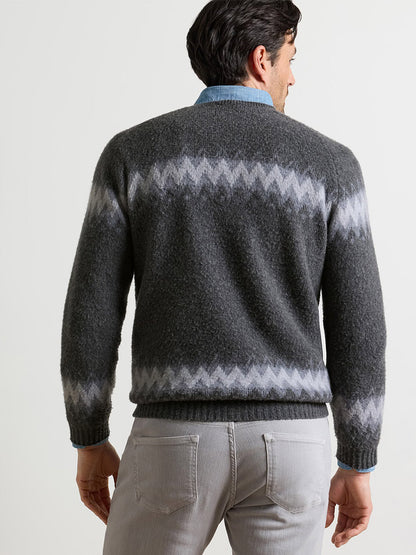 A person wearing a grey Peter Millar Après-Ski Crewneck Sweater in Fossil with a zig-zag pattern across the chest and cuffs, layered over a blue collared shirt.