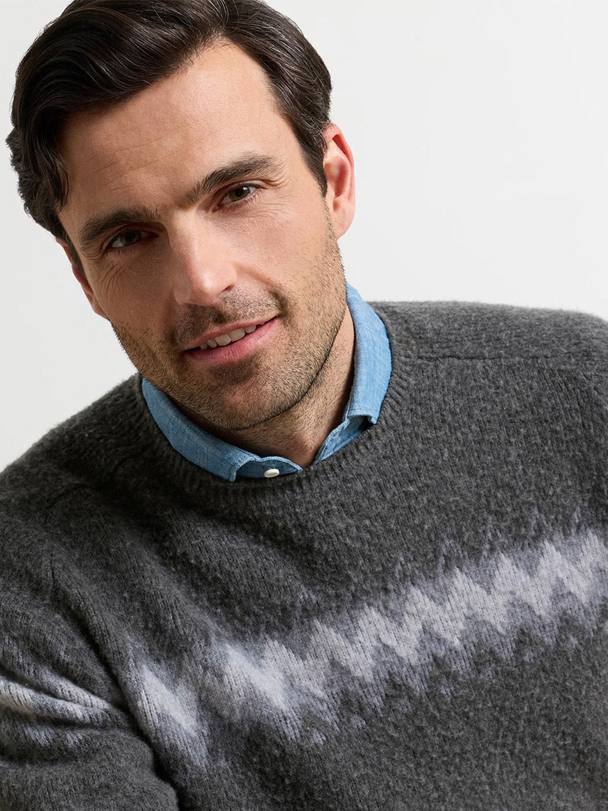 A man wearing a grey chevron-patterned Peter Millar Après-Ski Crewneck Sweater in Fossil over a blue collared shirt.